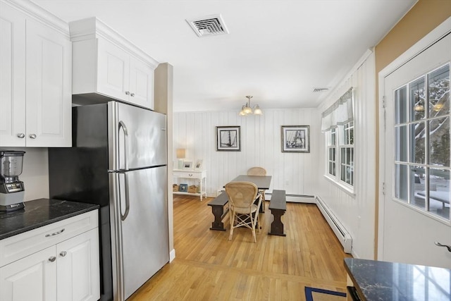 kitchen with a healthy amount of sunlight, white cabinets, stainless steel refrigerator, and dark stone counters