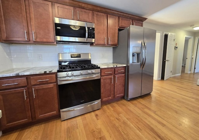 kitchen with tasteful backsplash, light hardwood / wood-style flooring, light stone countertops, and appliances with stainless steel finishes