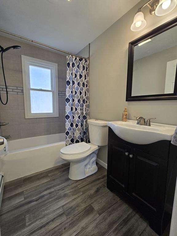 full bathroom with toilet, wood-type flooring, a baseboard radiator, vanity, and shower / bath combination with curtain