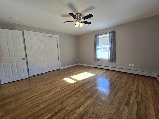 unfurnished bedroom featuring wood-type flooring, a baseboard heating unit, ceiling fan, and a closet