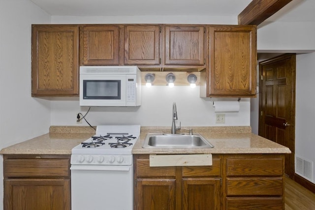 kitchen featuring light countertops, visible vents, brown cabinetry, a sink, and white appliances