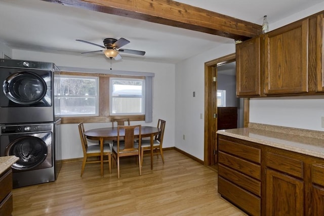 kitchen featuring ceiling fan, baseboards, light countertops, light wood finished floors, and stacked washer and clothes dryer