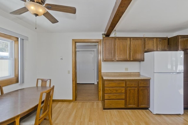 kitchen with light wood finished floors, brown cabinets, beamed ceiling, and freestanding refrigerator