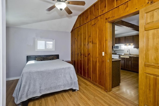 bedroom featuring lofted ceiling, light wood-style floors, baseboards, and a sink