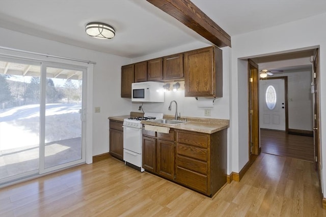 kitchen featuring light countertops, white appliances, a sink, and light wood-style floors