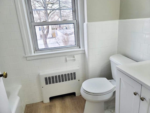 bathroom featuring vanity, radiator, hardwood / wood-style floors, and tile walls