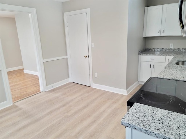 kitchen with electric range, light hardwood / wood-style flooring, light stone countertops, and white cabinets