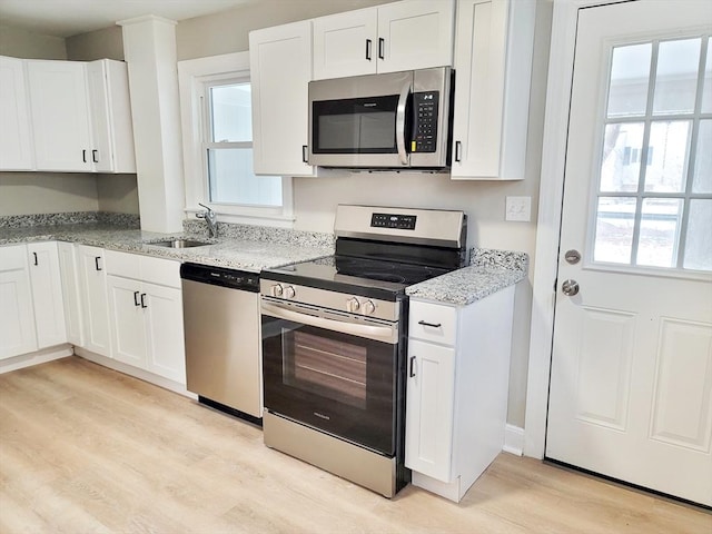 kitchen featuring appliances with stainless steel finishes, sink, white cabinets, light stone counters, and light hardwood / wood-style floors