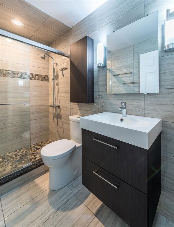 bathroom with tile walls, toilet, a tile shower, and vanity