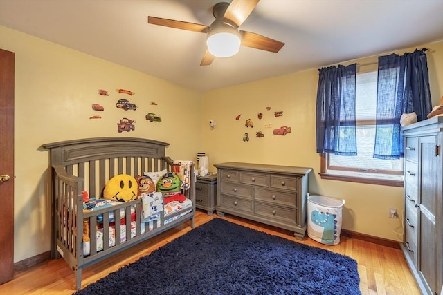 bedroom featuring light wood finished floors, baseboards, ceiling fan, and a crib
