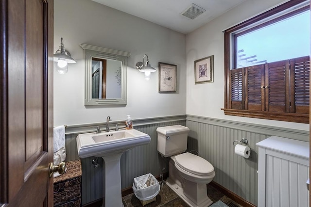 bathroom featuring toilet, visible vents, wainscoting, and a sink