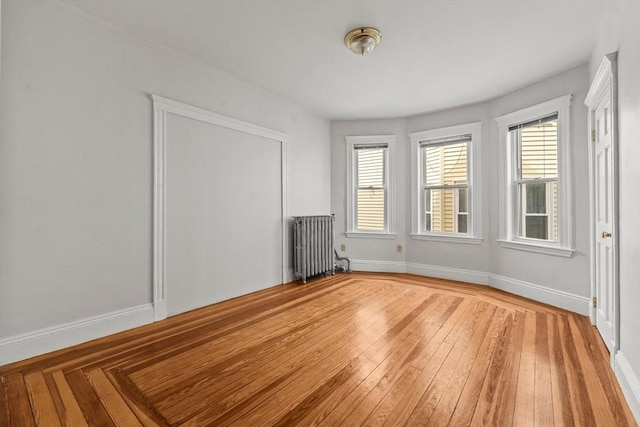 empty room with baseboards, radiator, light wood-style floors, and a wealth of natural light