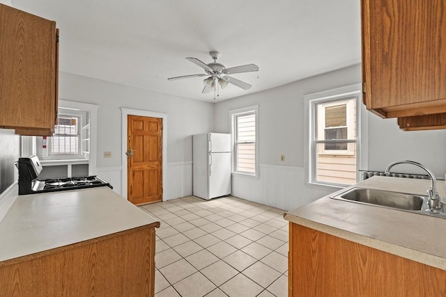 kitchen featuring freestanding refrigerator, wainscoting, ceiling fan, a sink, and gas stove