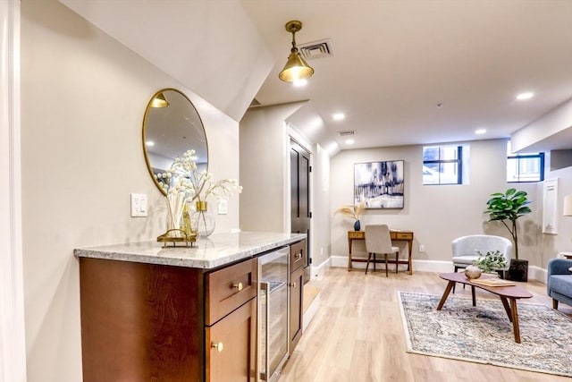 interior space with light stone countertops, light wood-type flooring, hanging light fixtures, and beverage cooler