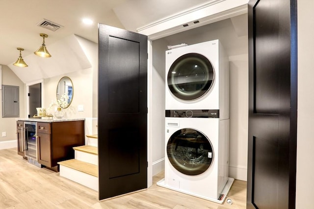 laundry area featuring electric panel, light wood-type flooring, wine cooler, and stacked washer and clothes dryer