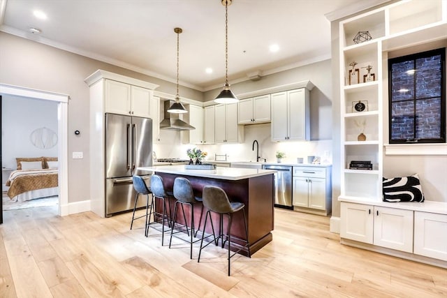 kitchen with white cabinets, sink, wall chimney exhaust hood, appliances with stainless steel finishes, and decorative light fixtures