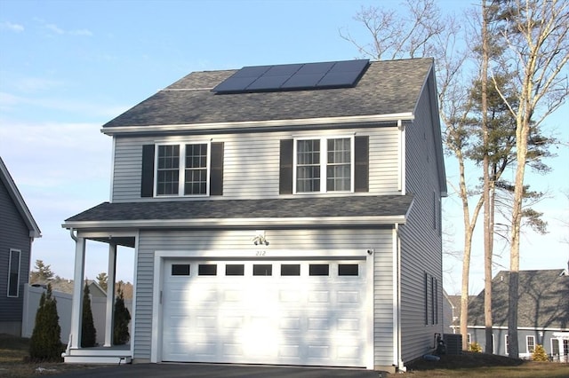 view of front facade featuring driveway, a garage, roof mounted solar panels, and roof with shingles