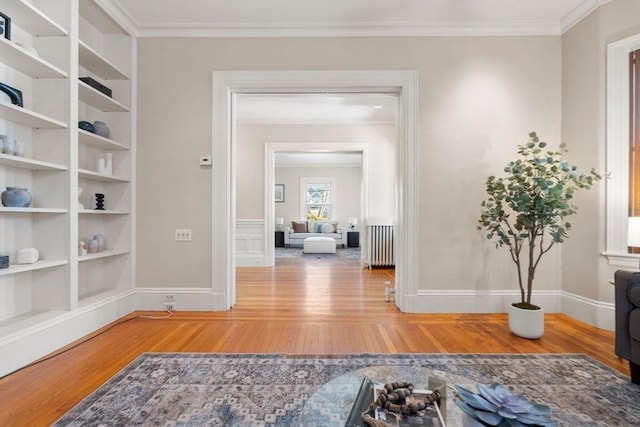 hallway with built in shelves, radiator heating unit, ornamental molding, and wood-type flooring