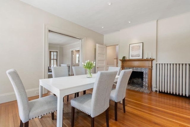 dining room featuring radiator, a fireplace, hardwood / wood-style floors, and ornamental molding