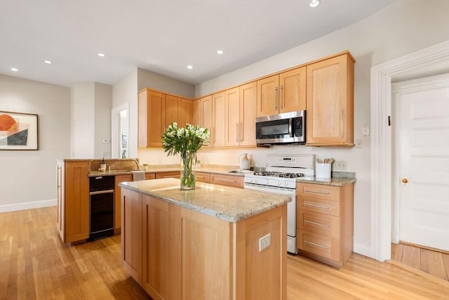 kitchen featuring light stone countertops, a center island, white range with gas cooktop, and light brown cabinets