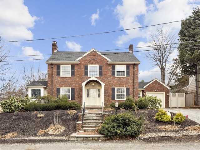 colonial home featuring fence, driveway, an attached garage, a chimney, and brick siding