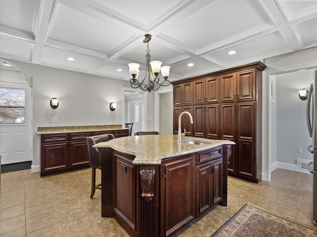 kitchen with decorative light fixtures, an island with sink, arched walkways, coffered ceiling, and a sink