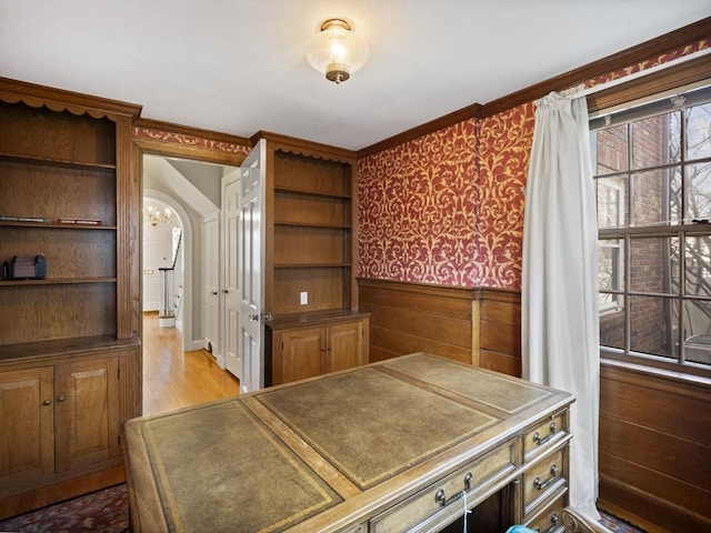 interior space featuring wallpapered walls, wainscoting, light wood-style flooring, arched walkways, and a notable chandelier