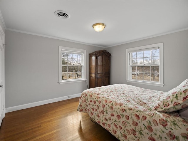 bedroom with wood finished floors, visible vents, baseboards, and ornamental molding