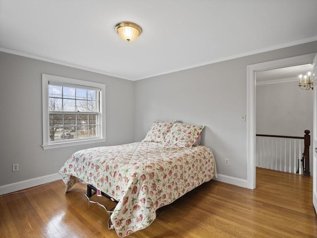 bedroom featuring a notable chandelier, ornamental molding, baseboards, and wood finished floors