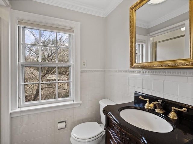 half bath with toilet, ornamental molding, tile walls, wainscoting, and vanity