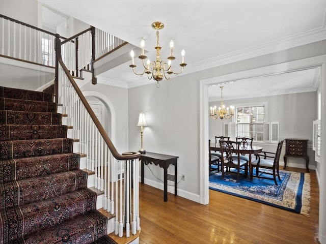 staircase featuring wood finished floors, baseboards, arched walkways, ornamental molding, and a chandelier