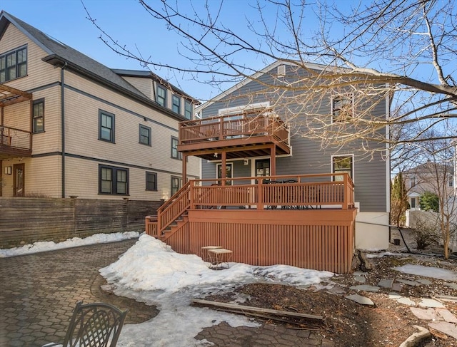 snow covered back of property with a deck and stairs