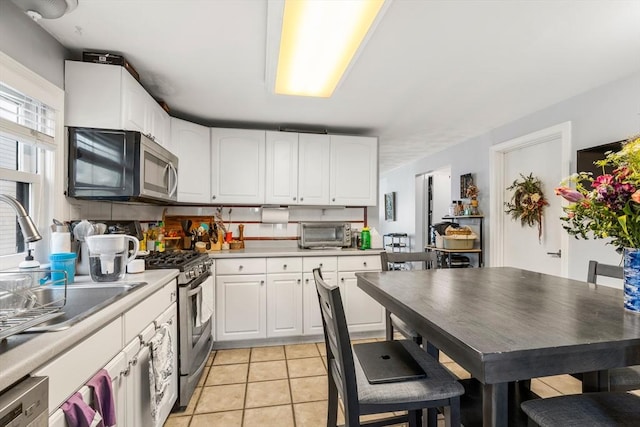 kitchen featuring a toaster, light countertops, appliances with stainless steel finishes, light tile patterned flooring, and white cabinetry