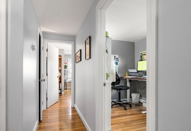 corridor with a baseboard radiator, baseboards, and wood finished floors