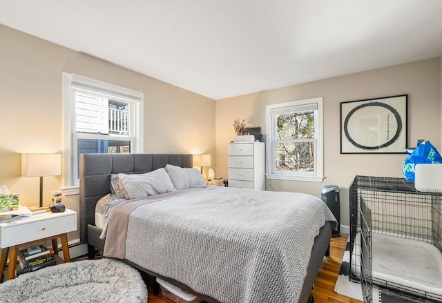 bedroom with multiple windows, wood finished floors, baseboards, and baseboard heating