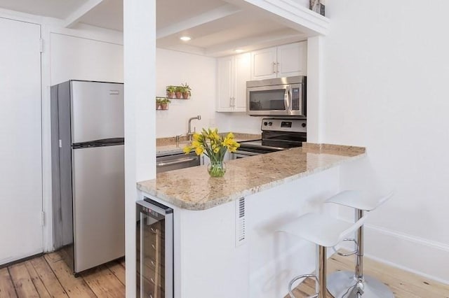 kitchen with stainless steel appliances, beverage cooler, light wood-type flooring, white cabinetry, and a kitchen bar