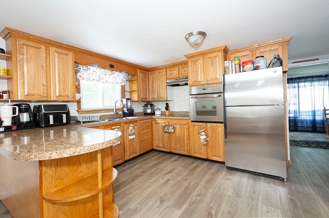 kitchen featuring tasteful backsplash, kitchen peninsula, stainless steel appliances, light hardwood / wood-style flooring, and sink