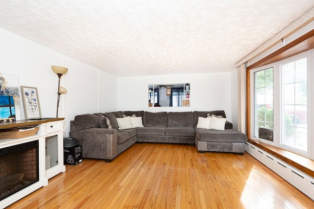 living room with a baseboard heating unit, a textured ceiling, and light wood-type flooring