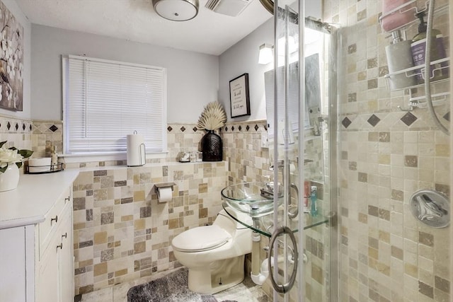 bathroom with tile walls, an enclosed shower, vanity, and toilet