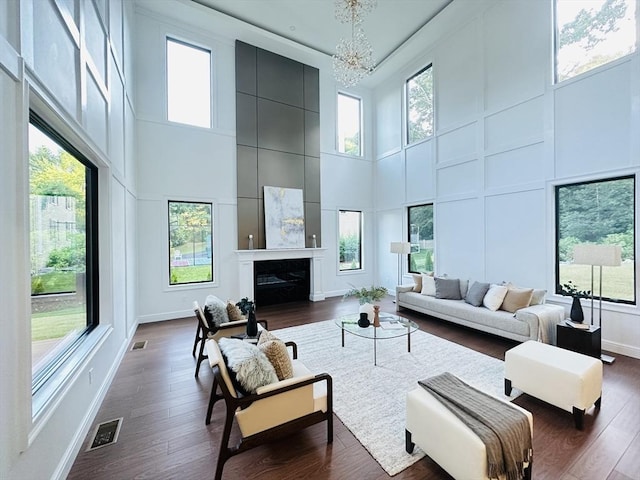 living room with a large fireplace, dark hardwood / wood-style flooring, a towering ceiling, and a chandelier