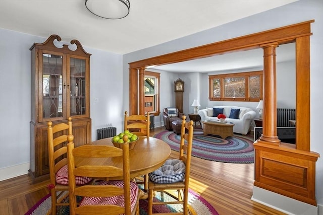 dining space with ornate columns, hardwood / wood-style floors, a healthy amount of sunlight, and radiator heating unit