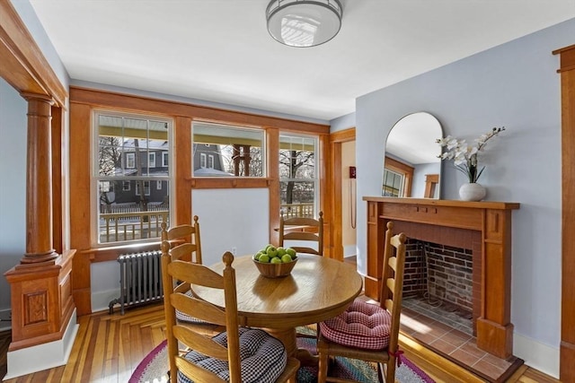 dining space featuring radiator, light hardwood / wood-style flooring, a tile fireplace, and ornate columns