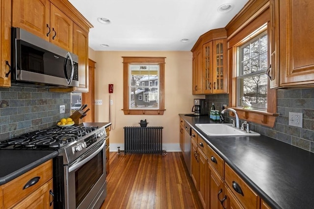 kitchen with appliances with stainless steel finishes, radiator heating unit, sink, backsplash, and dark hardwood / wood-style flooring