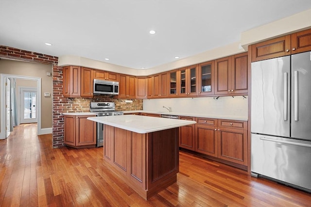 31 Millmont St Unit 1, Boston, MA 02119 - kitchen featuring brown cabinets, appliances with stainless steel finishes, light countertops, glass insert cabinets, and hardwood / wood-style flooring