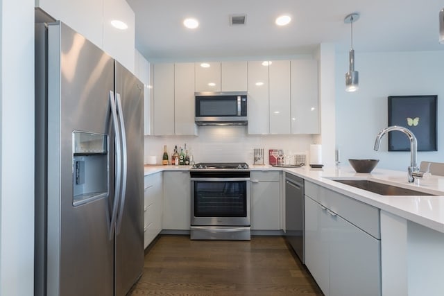 kitchen featuring appliances with stainless steel finishes, sink, dark hardwood / wood-style flooring, hanging light fixtures, and white cabinetry