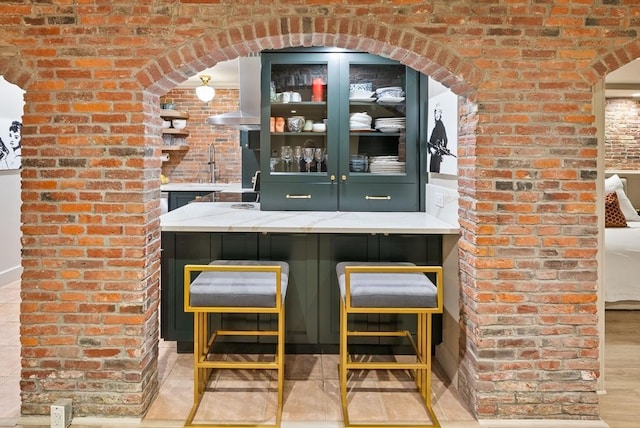 bar featuring wall chimney range hood, wood finished floors, brick wall, and a sink