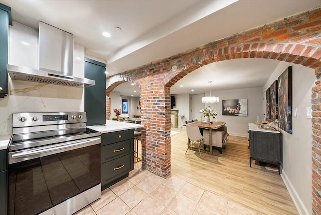 kitchen featuring arched walkways, stainless steel electric range, light countertops, and exhaust hood