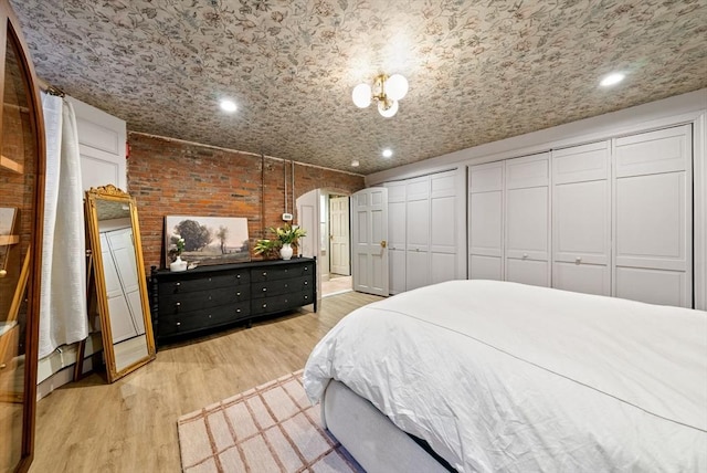 bedroom featuring multiple closets, recessed lighting, arched walkways, light wood-style floors, and brick wall