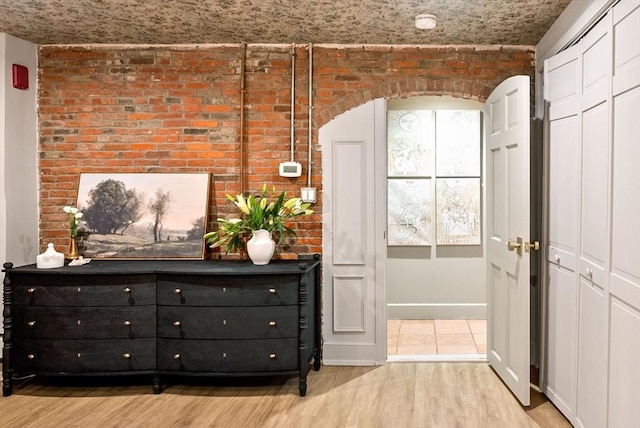 interior space with baseboards, arched walkways, wood finished floors, and brick wall