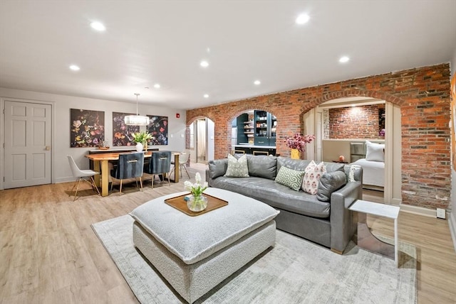 living area with recessed lighting, light wood-type flooring, arched walkways, and brick wall